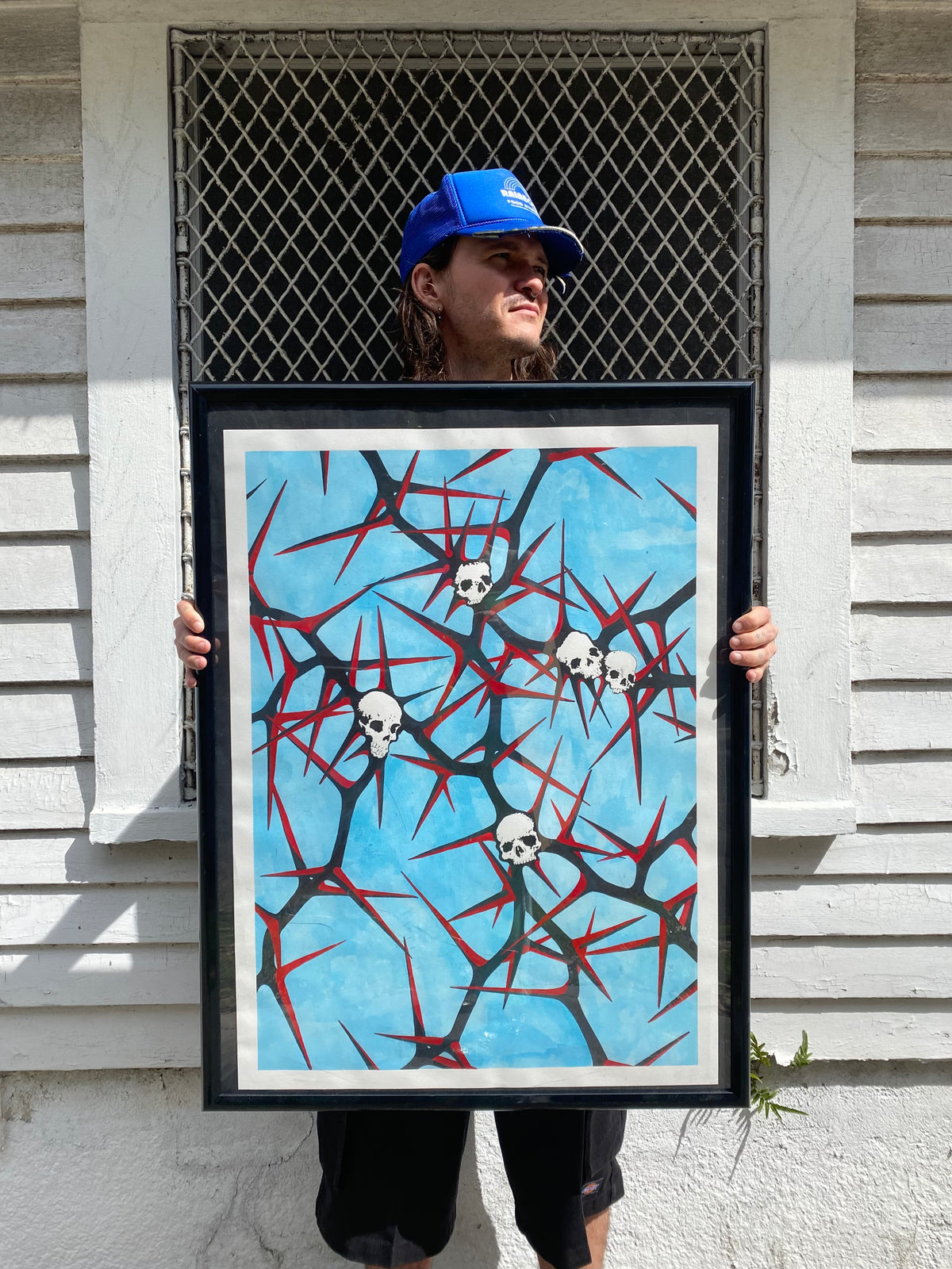 Papayo holding a framed artwork with skulls and branching red shapes