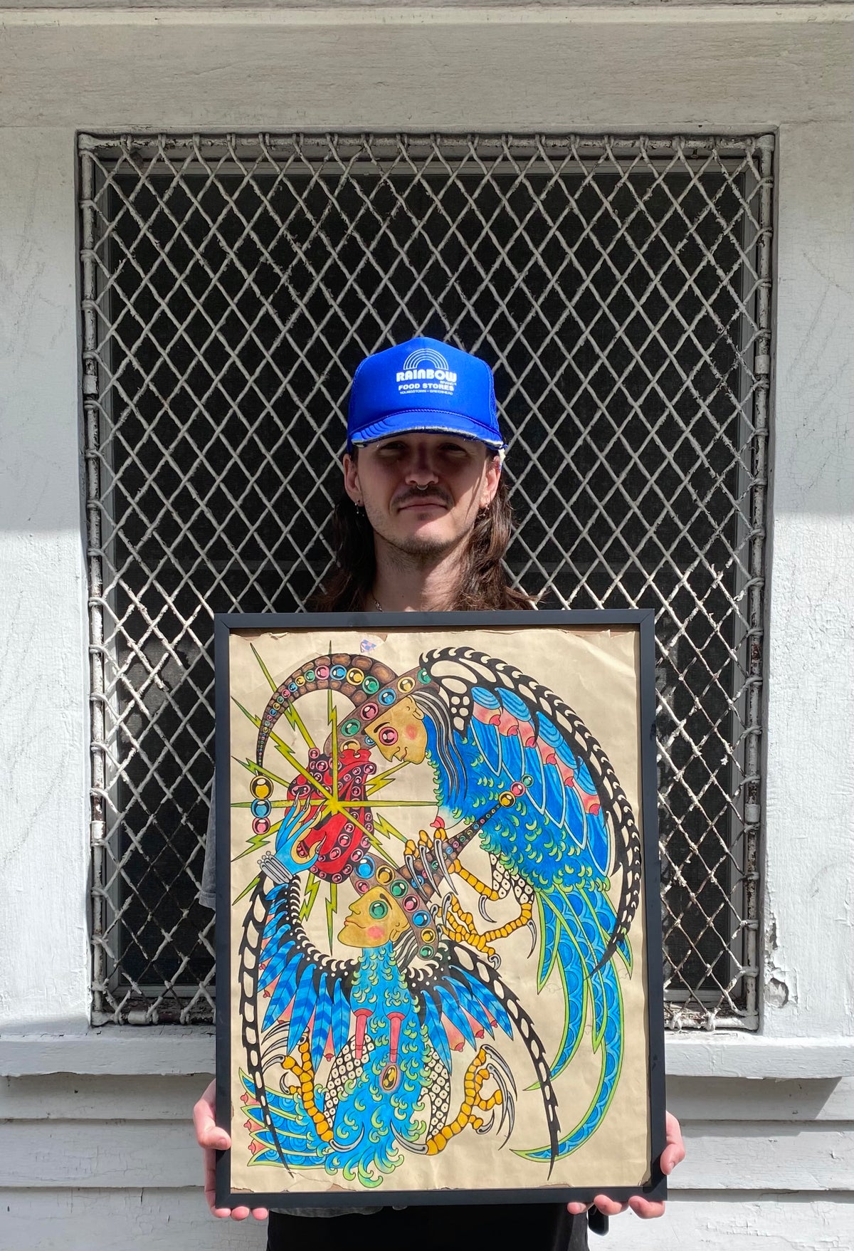 Papayo holding a framed artwork of a colorful winged figure
